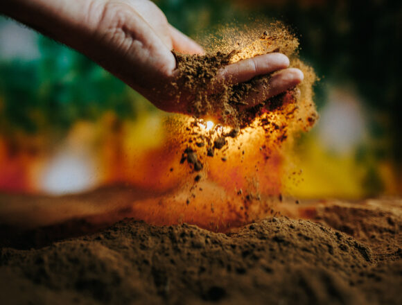 Hands releasing soil in a vibrant natural setting during daylight hours Βιοδυναμικά Παρασκευάσματα: Λίγη Ύλη – Μεγάλη Επίδραση