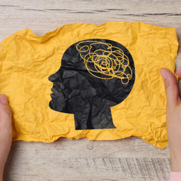 A female hand holds a crumpled paper with a black silhouette of Η ψυχική υγεία στον ΟΗΕ: ένα νέο παγκόσμιο αφήγημα και οι σκιές του